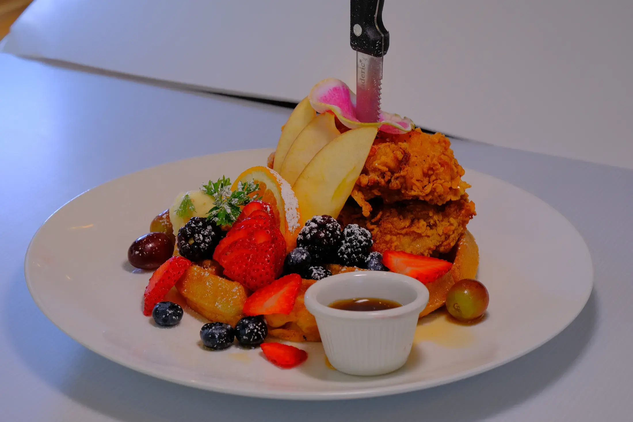 Fried chicken over a waffle with strawberries, blackberries, grapes and a pot of syrup