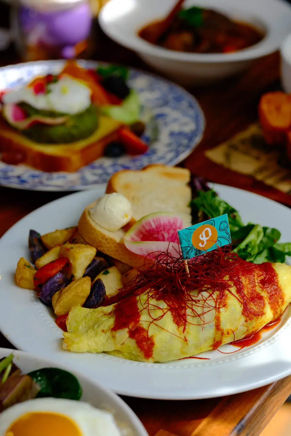 A folded omelette with chilli threads, beside breakfast potatoes, toast and greens