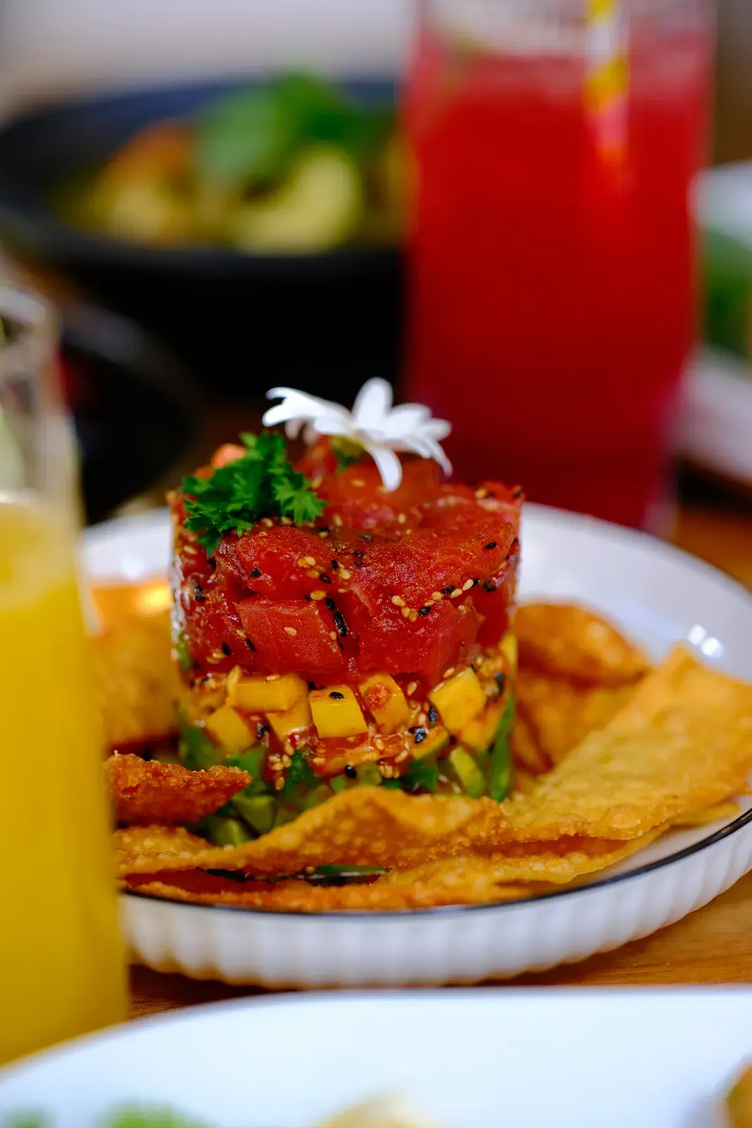 A stacked tartare tower with crisps beside a glass of orange juice