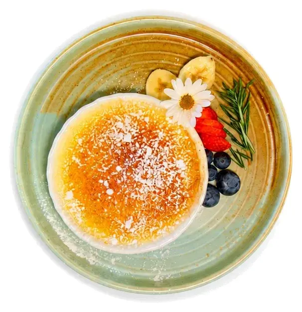 A sugar-dusted pancake with banana, strawberry and blueberries in a green bowl