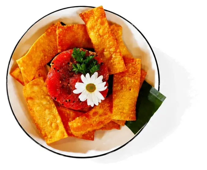 Tortilla chips arranged around a tomato and a flower in a black-rimmed bowl