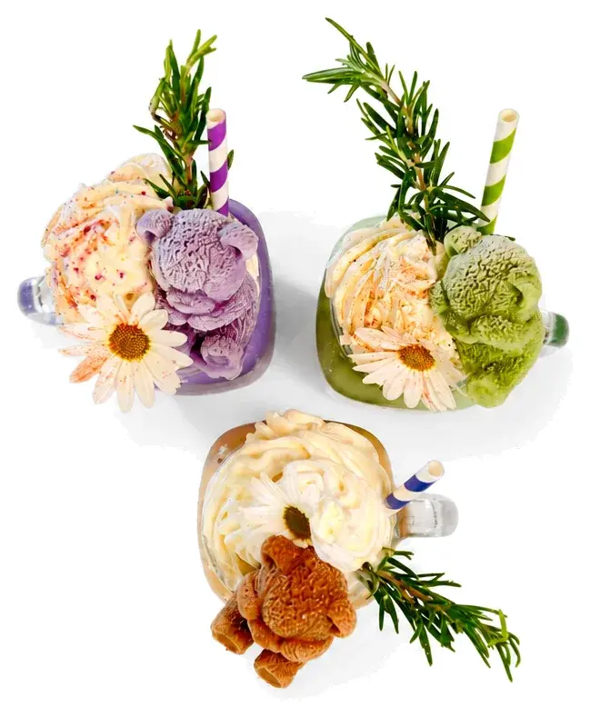 Three tall drinks topped with cream, flowers and rosemary